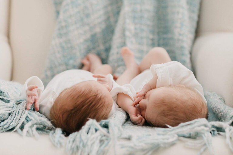 Two newborn babies sleeping on a blanket